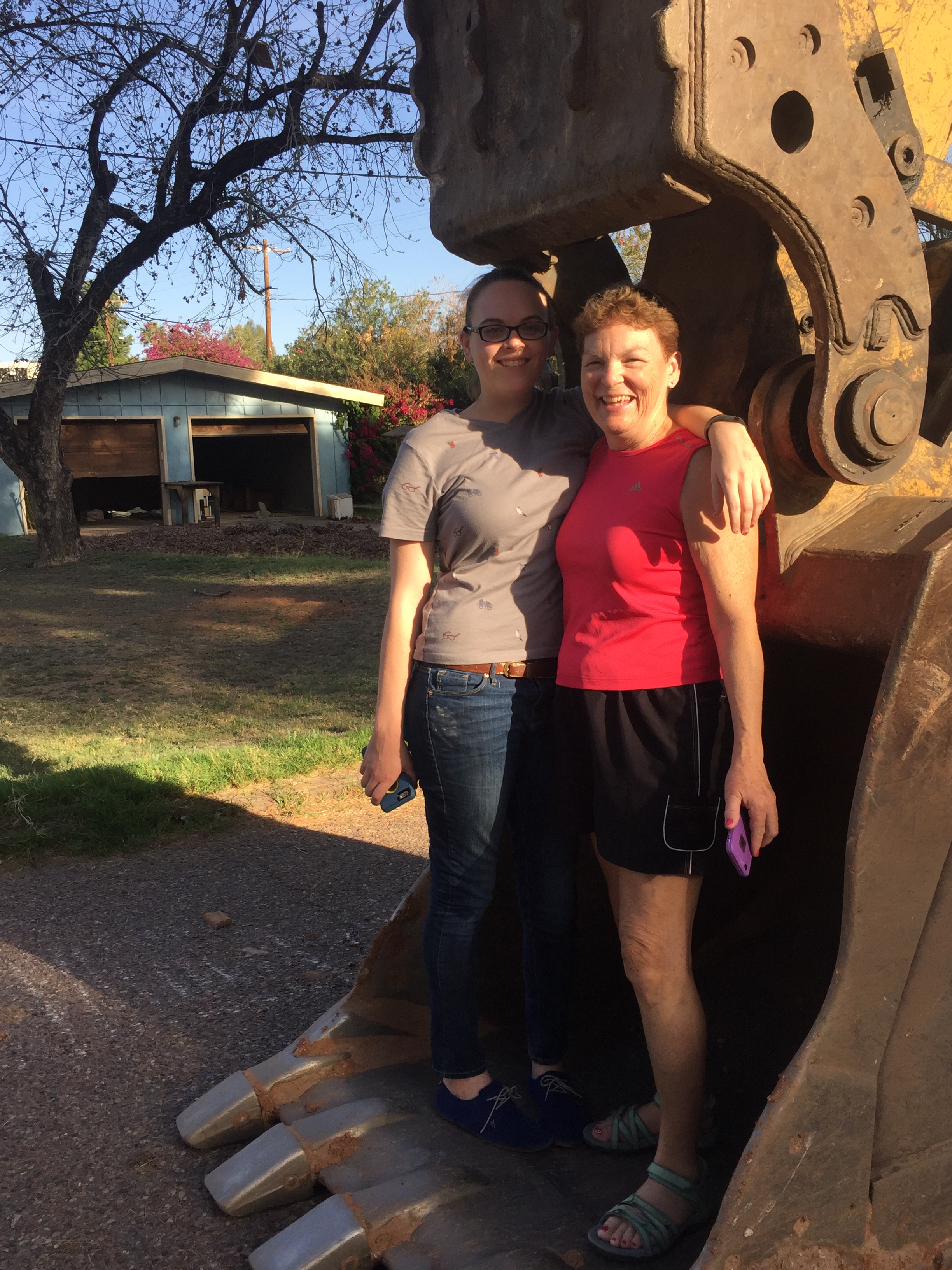 Ariel and Lesley standing in the bucket of a front loader at the old house.